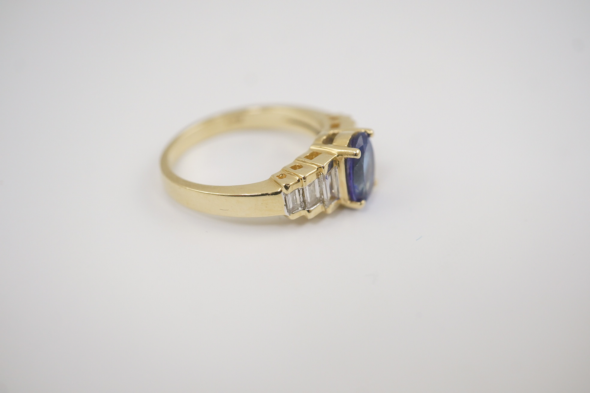 A modern 14k gold and single stone oval cut tanzanite set dress ring, with six stone graduated baguette cut diamond set shoulders